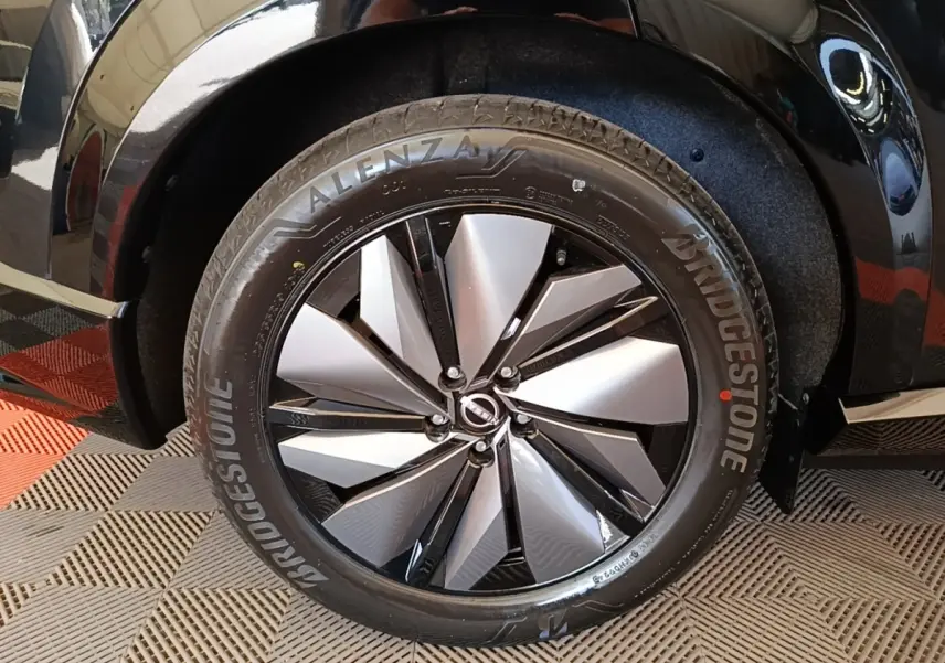 Gros plan sur la roue avant droite du Nissan Ariya noir, mettant en valeur la jante alu bicolore et le pneu Bridgestone.