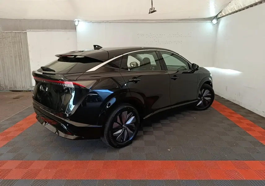 Nissan Ariya 63kWh noir en 3/4 arrière droit, avec feux arrière LED et jantes aérodynamiques dans un garage.