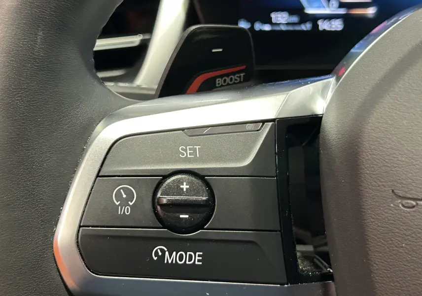 Gros plan sur les commandes de régulateur de vitesse au volant cuir du BMW X1 Spacesilber 2024, finition M Sport.
