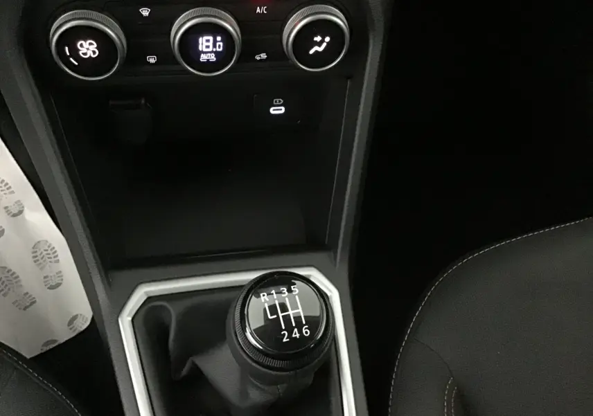 Gros plan sur la commande de boîte manuelle noire et la climatisation digitale à 18°C dans une Dacia Sandero Stepway kaki 2025.