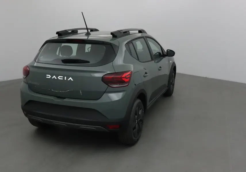 Vue 3/4 arrière droite d'une Dacia Sandero Stepway 2025 kaki Kichen avec barres de toit et feux arrière allumés.