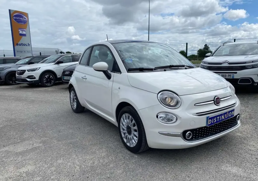 Vue 3/4 avant d'une Fiat 500 blanche avec jantes alliage 16'' Spider et toit panoramique visible.