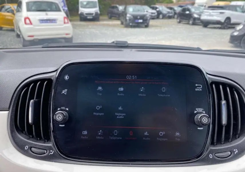 Écran tactile central du tableau de bord du Fiat 500 blanc, avec commandes multimédia et aérateurs latéraux visibles.