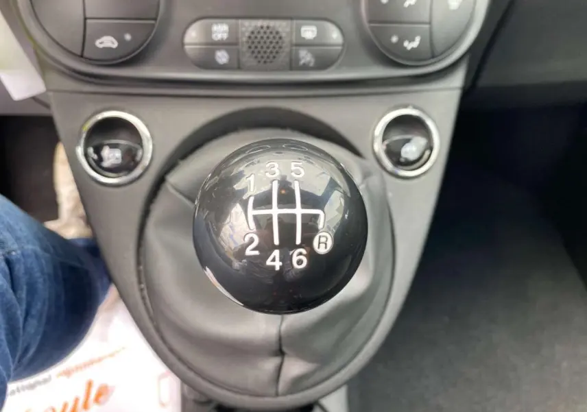 Gros plan sur le levier de vitesses manuel noir de la FIAT 500 2024, avec commandes climatisation en arrière-plan.