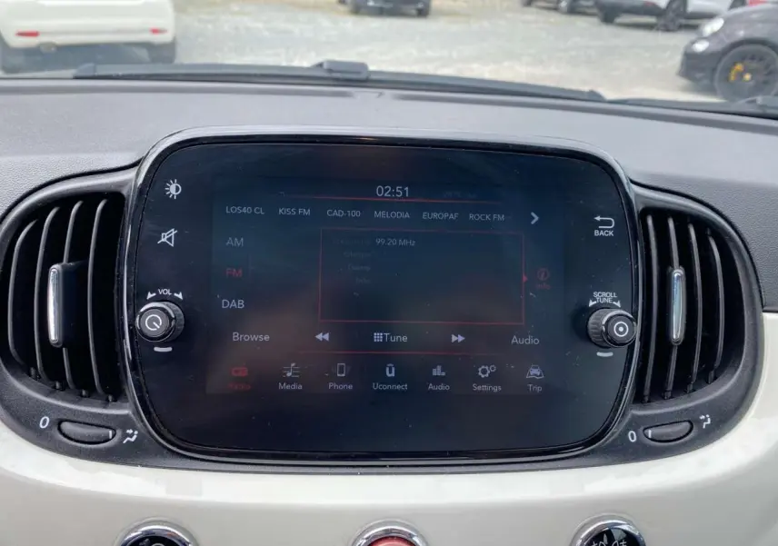 Vue rapprochée de l’écran tactile central du tableau de bord blanc d’une Fiat 500 2024 avec commandes audio et climatisation.