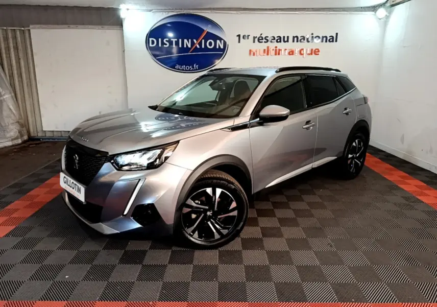 Peugeot 2008 gris clair en 3/4 avant droit, avec jantes noires et toit noir, dans un showroom intérieur.