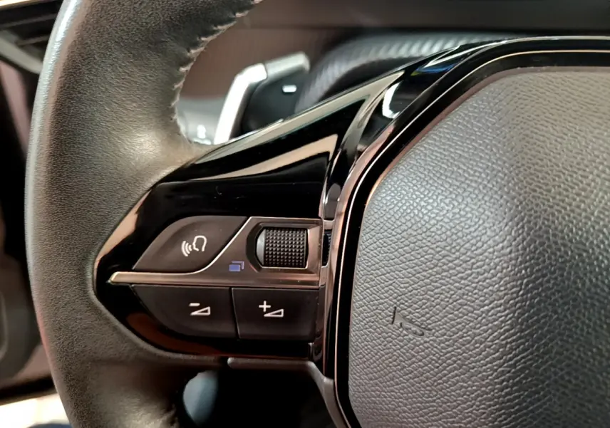 Gros plan sur les commandes gauche du volant cuir noir du Peugeot 2008 gris clair, avec boutons multifonctions et molette.
