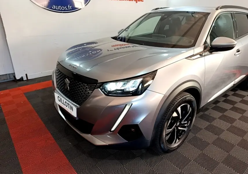Peugeot 2008 gris clair en 3/4 avant droit, phares LED allumés et jantes noires distinctives.