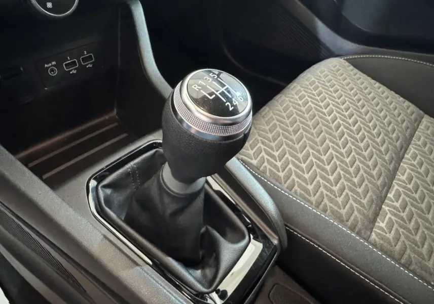 Gros plan sur le levier de vitesses manuel noir et argenté, avec siège tissu gris à motifs à droite dans une Renault Clio blanche.