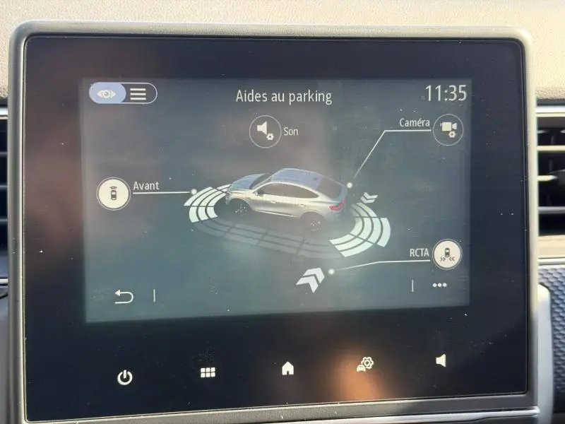Écran tactile intérieur montrant l'aide au parking du Renault Arkana 2025 avec vue 3/4 arrière du véhicule gris métallisé.
