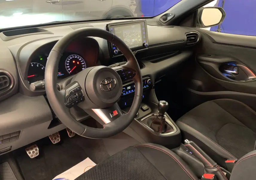 Vue intérieure côté conducteur de la Toyota Yaris 1.6 VVT-I 261 Premium GR avec volant cuir et levier de vitesse manuel.