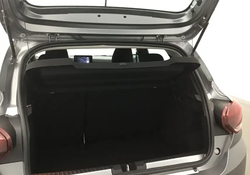 Coffre ouvert vu de l'arrière droit d'une Dacia Sandero Stepway 2025 gris schiste, intérieur noir visible.