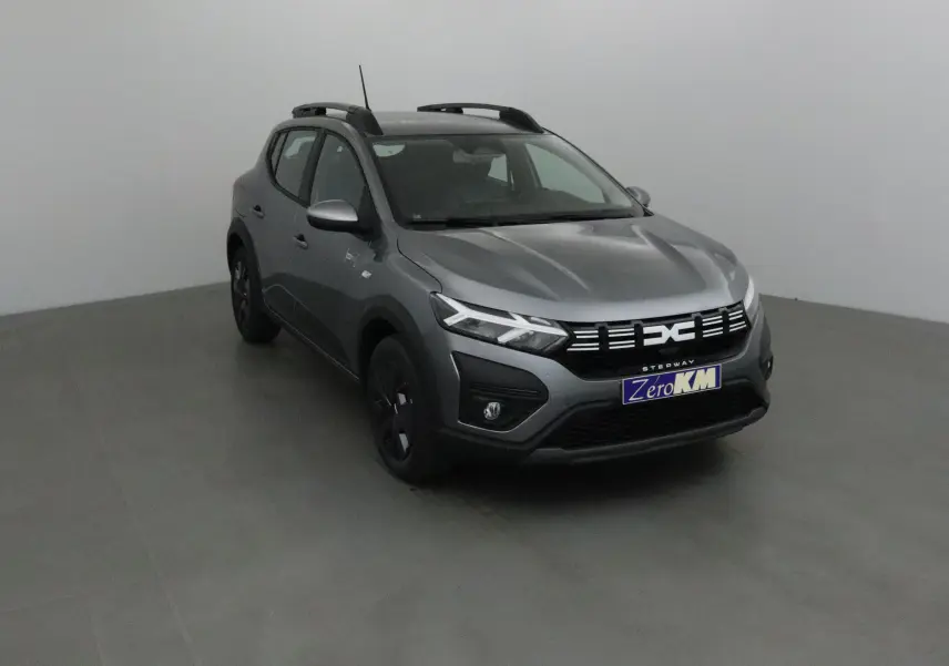 Dacia Sandero Stepway gris schiste vue 3/4 avant droit avec calandre moderne et barres de toit noires.