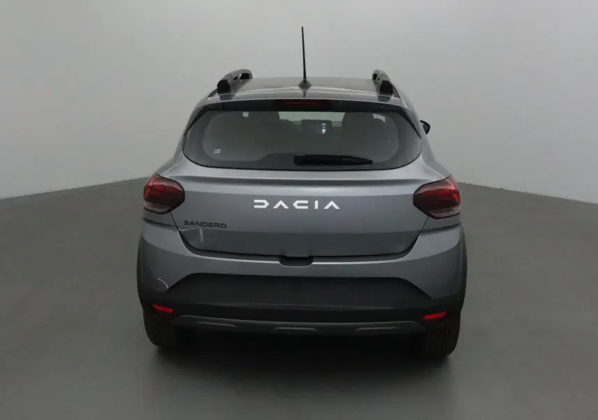 Vue arrière d'une Dacia Sandero Stepway gris schiste avec barres de toit et feux arrière allumés.