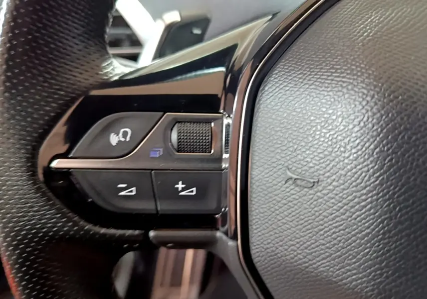 Gros plan sur les commandes gauche du volant cuir noir du Peugeot 3008 GT bleu, avec molette et boutons multifonctions.
