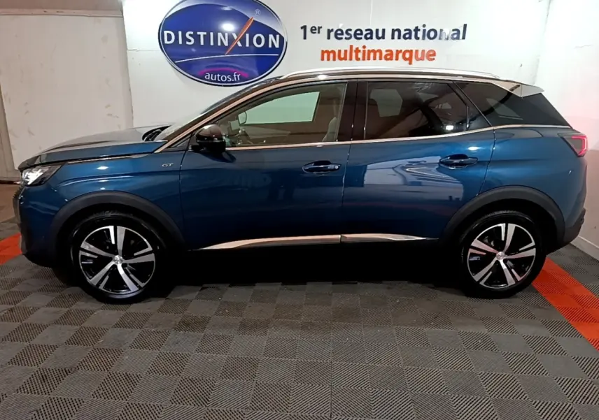 Vue latérale droite d'un Peugeot 3008 GT bleu 2021 avec jantes alliage et toit noir en intérieur showroom.