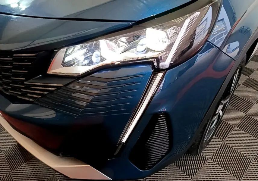 Gros plan sur l'avant droit bleu du Peugeot 3008 2021, mettant en valeur le phare LED et la calandre stylisée.