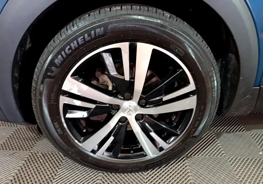 Gros plan sur la roue avant gauche du Peugeot 3008 bleu, avec jante alliage bicolore et pneu Michelin.
