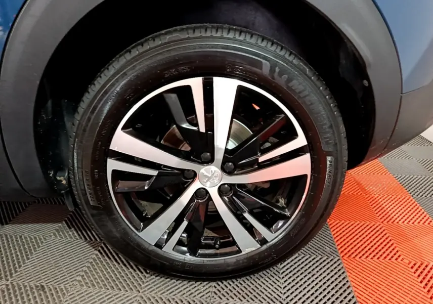 Gros plan sur la roue avant droite du Peugeot 3008 bleu, avec jante alliage bicolore noire et argentée.