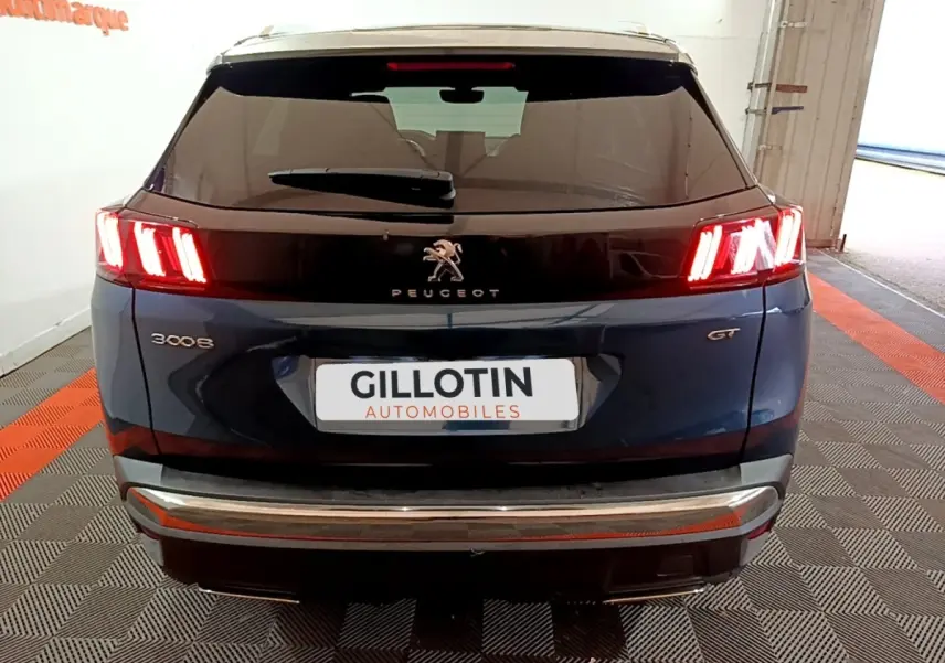 Vue arrière d'un Peugeot 3008 GT bleu avec feux LED allumés et bandeau noir brillant sur le hayon.