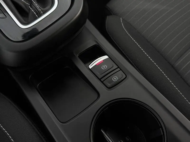 Gros plan sur la console centrale noire du Renault Arkana 2025, montrant les boutons de frein à main et auto hold, siège tissu gris à droite.