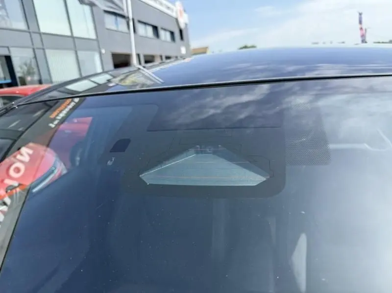 Gros plan sur le pare-brise avant du Toyota C-HR Hybride bleu persan 2024, avec reflet du ciel et bâtiment en arrière-plan.