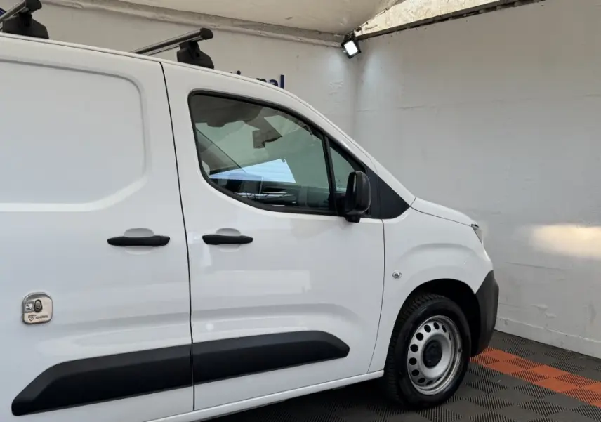 Vue latérale droite d’un Peugeot Partner blanc avec protections noires sur portes et jante acier simple.