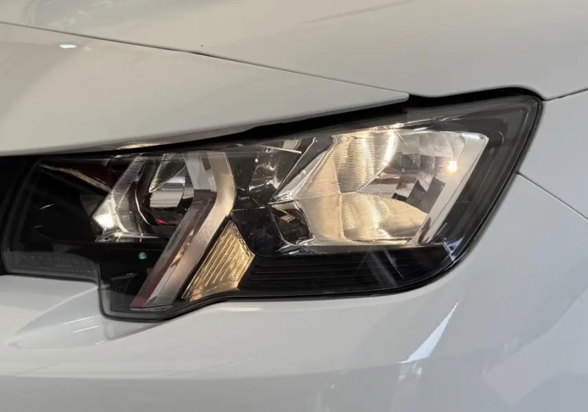 Gros plan sur le phare avant droit du Peugeot Partner blanc, mettant en valeur ses détails lumineux et la carrosserie.