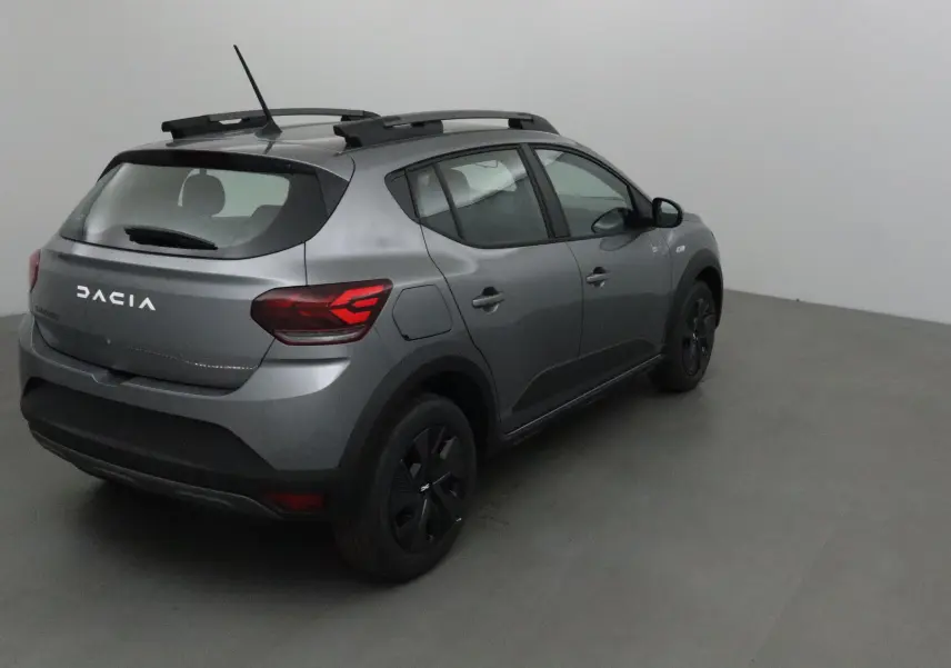 Vue 3/4 arrière droite d'une Dacia Sandero Stepway 2025 gris schiste avec barres de toit et feux arrière LED distinctifs.