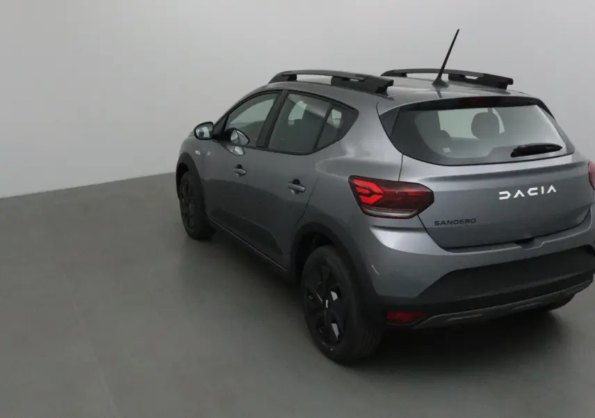Vue 3/4 arrière droite d'une Dacia Sandero Stepway 2025 gris schiste avec barres de toit et feux arrière LED.