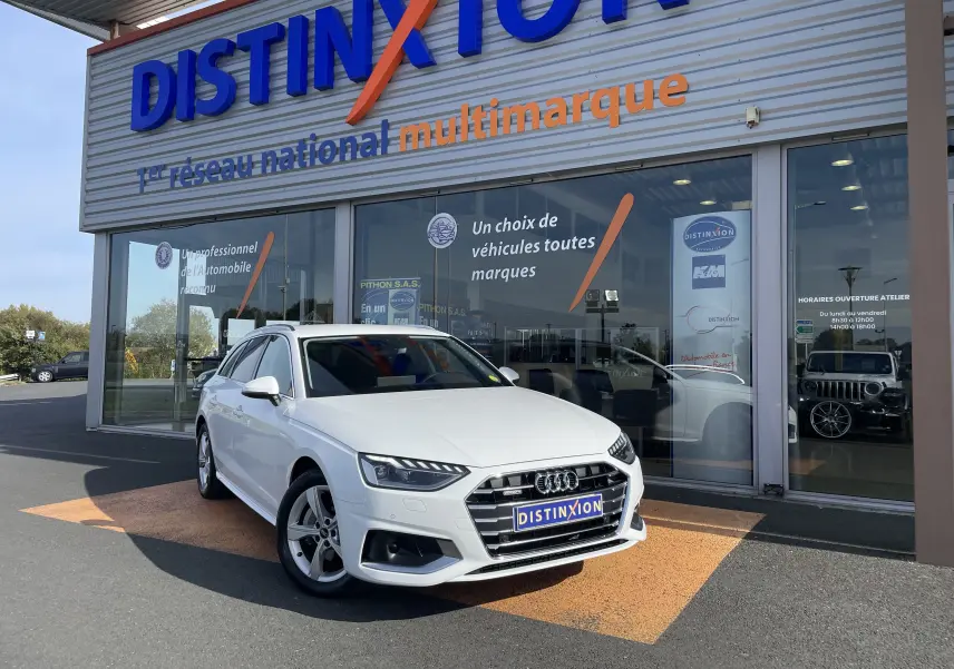 Audi A4 Avant blanc vue 3/4 avant droit, stationnée devant un showroom Distinxion avec logo visible.