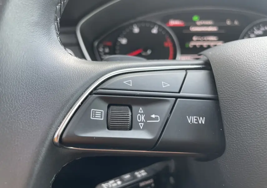 Gros plan sur les commandes gauche au volant d'une Audi A4 Avant 40 TDI 2022, avec tableau de bord flou en arrière-plan.