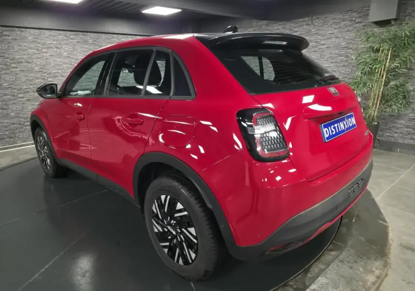 Vue 3/4 arrière droite d'un FIAT 600 rouge avec jantes bicolores et feux arrière LED dans un showroom.