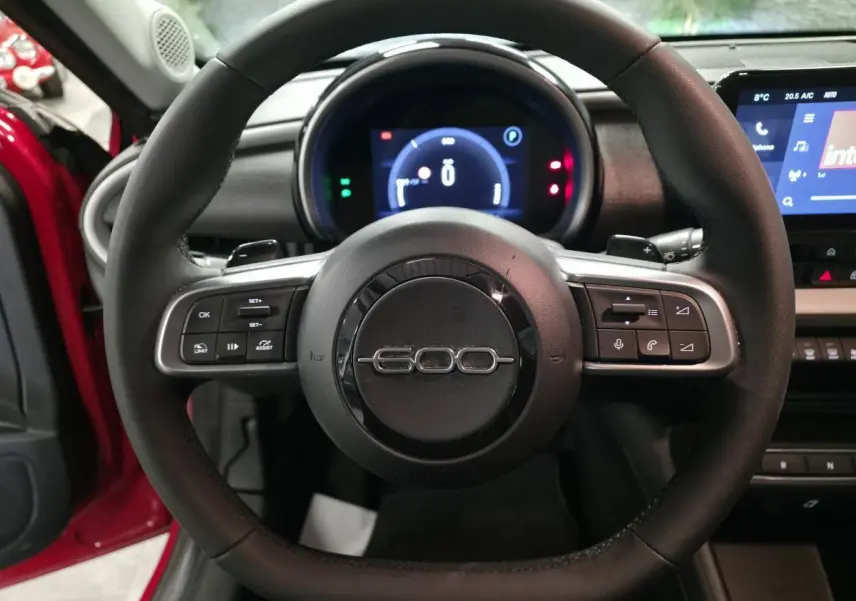 Vue centrée sur le volant noir avec logo 600, tableau de bord numérique et portière rouge visible côté gauche.