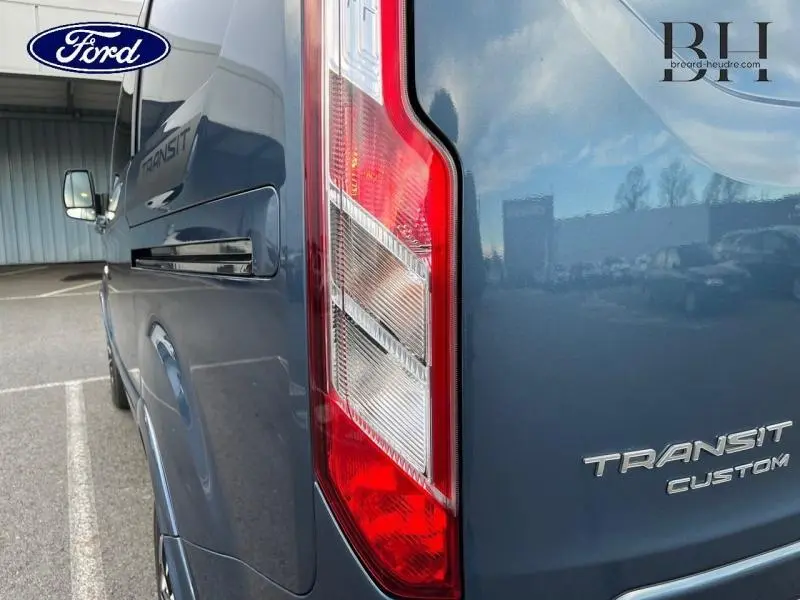 Gros plan sur l'arrière droit bleu azur métallisé du Ford Transit Custom avec feu arrière et logo visible.