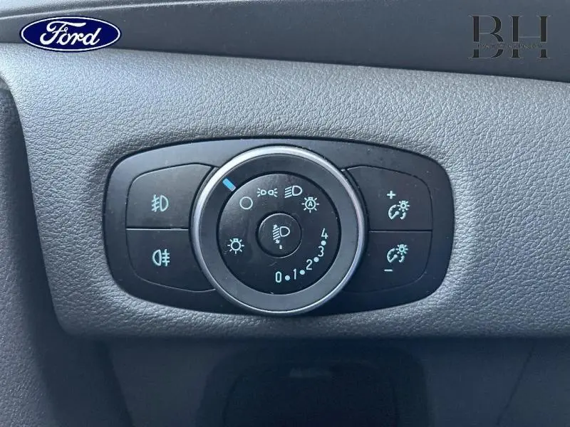 Gros plan sur la molette de réglage des phares et des feux du Ford Transit Custom Fourgon, tableau de bord noir.