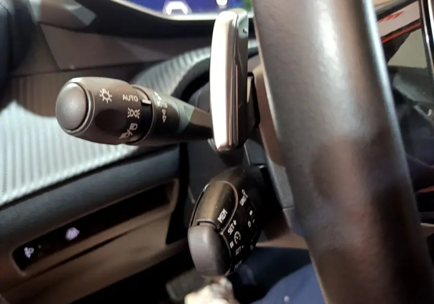 Gros plan sur les commandes au volant côté gauche du Peugeot 2008 orange, montrant les leviers de feux et régulateur de vitesse.