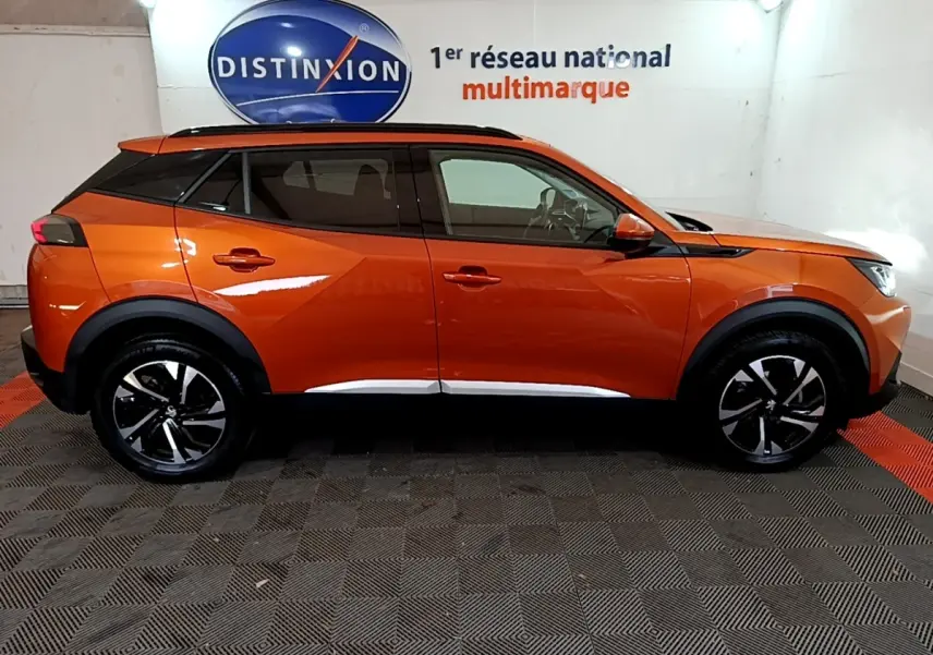 Vue de profil côté gauche d’un Peugeot 2008 orange avec jantes noires et toit noir dans un showroom.