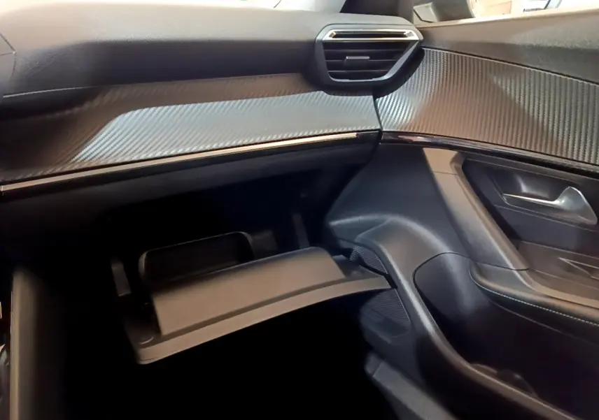 Intérieur côté passager du Peugeot 2008 2021, tableau de bord noir avec finition carbone et boîte à gants ouverte.