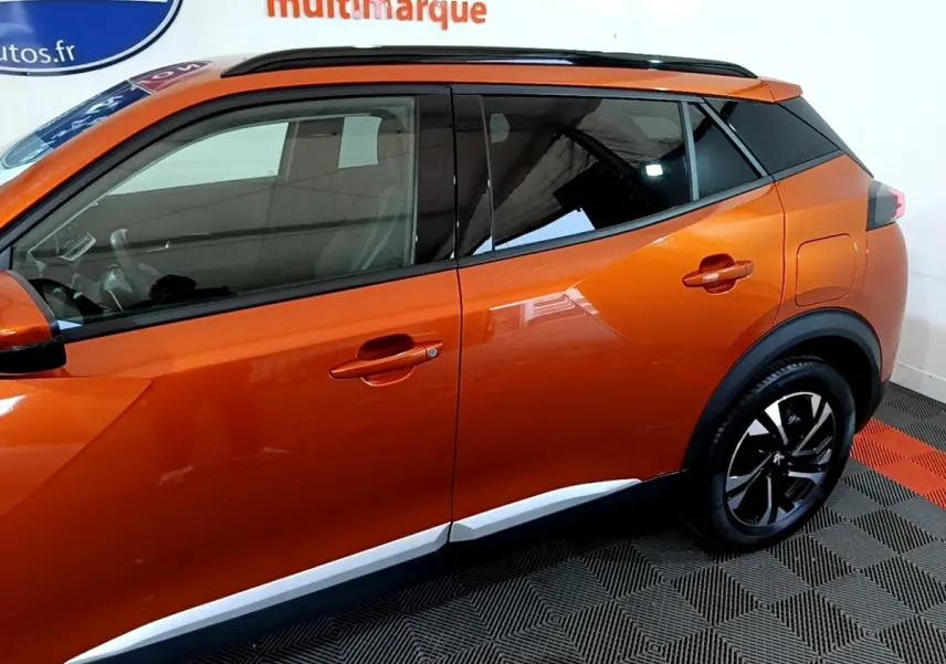 Vue de profil côté gauche du Peugeot 2008 orange 2021 avec jantes noires et toit noir contrasté.