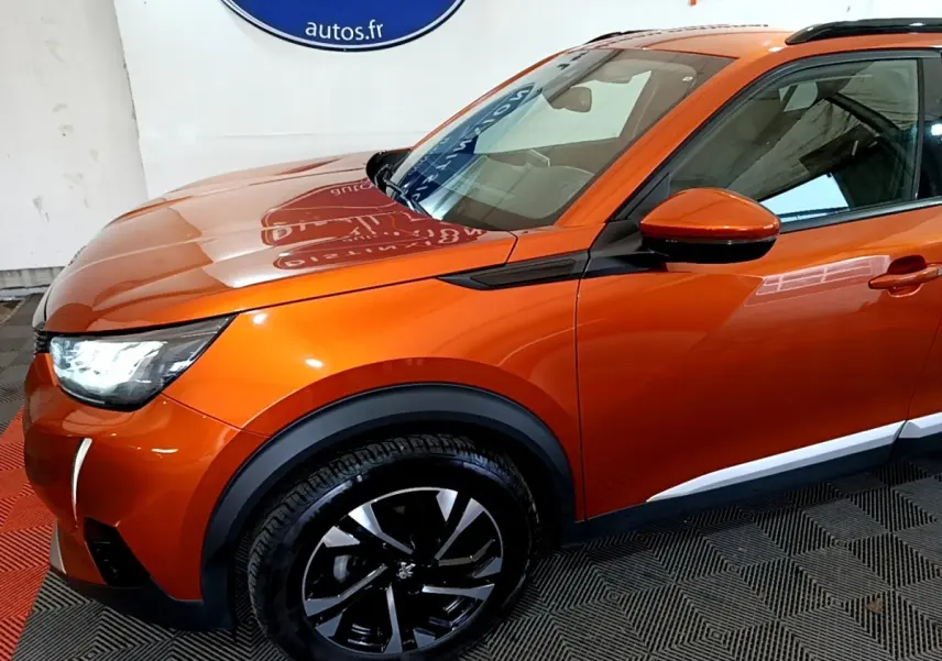 Peugeot 2008 orange vue 3/4 avant droit, avec phares LED allumés et jantes alliage noires distinctives.