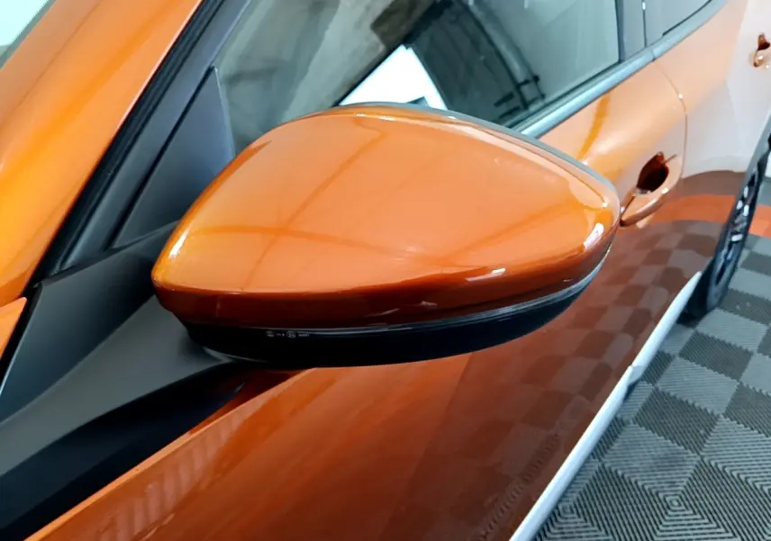 Gros plan sur le rétroviseur côté gauche orange brillant d’un Peugeot 2008 2021, avec partie de la portière visible.