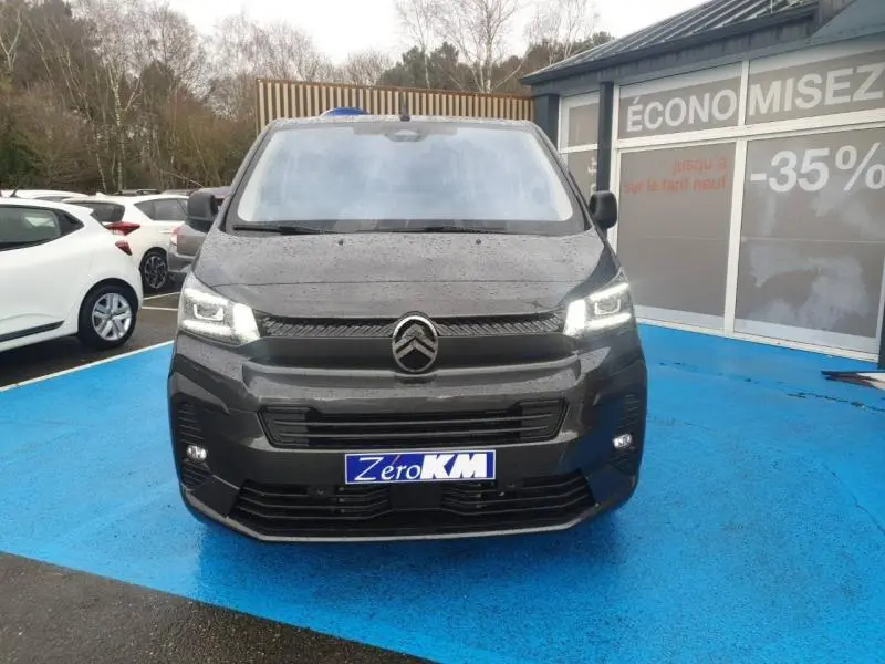Vue avant d'un Citroën Jumpy gris titane métal avec projecteurs LED allumés sur parking bleu.