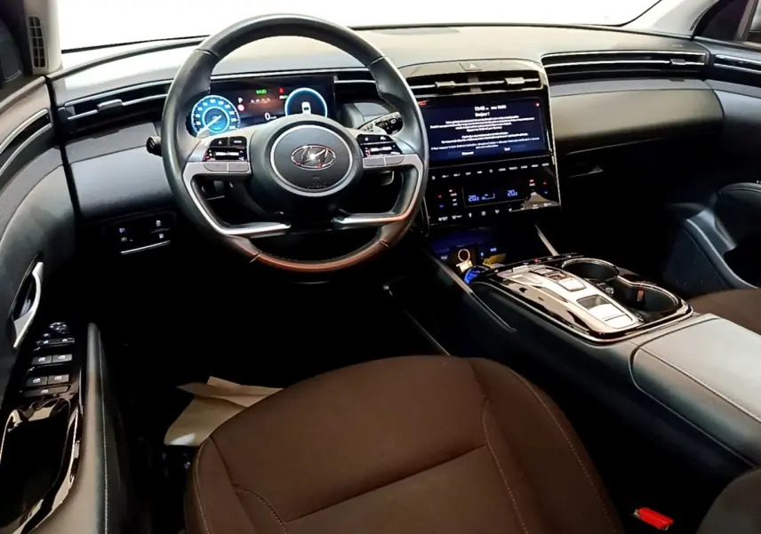 Vue intérieure avant du Hyundai Tucson 2023, tableau de bord noir avec écran tactile central et volant multifonctions.