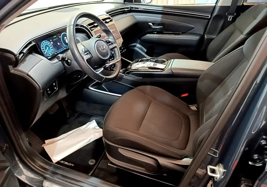 Vue intérieure côté conducteur du Hyundai Tucson bleu 2023, mettant en valeur le tableau de bord digital et la sellerie noire.