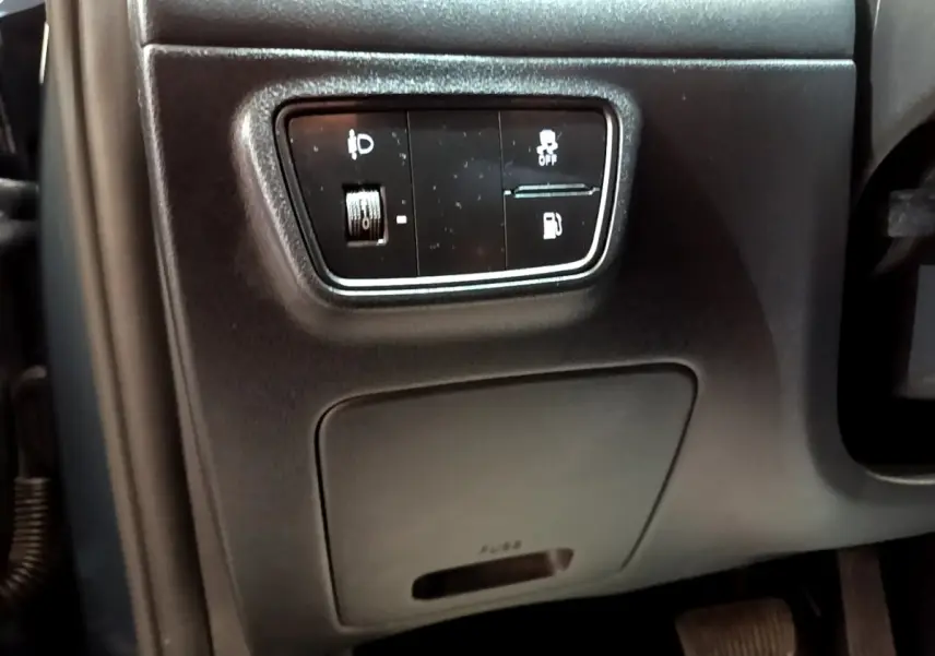 Gros plan sur les commandes noires côté gauche du tableau de bord du Hyundai Tucson 2023, avec réglage phares et traction.