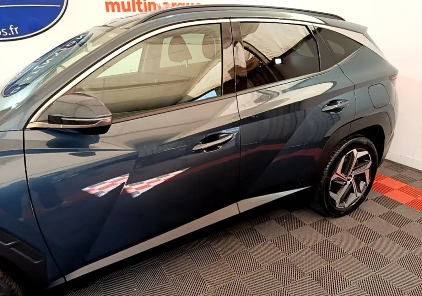 Vue latérale côté gauche d’un Hyundai Tucson bleu 2023 avec jantes au design moderne et rétroviseur noir brillant.