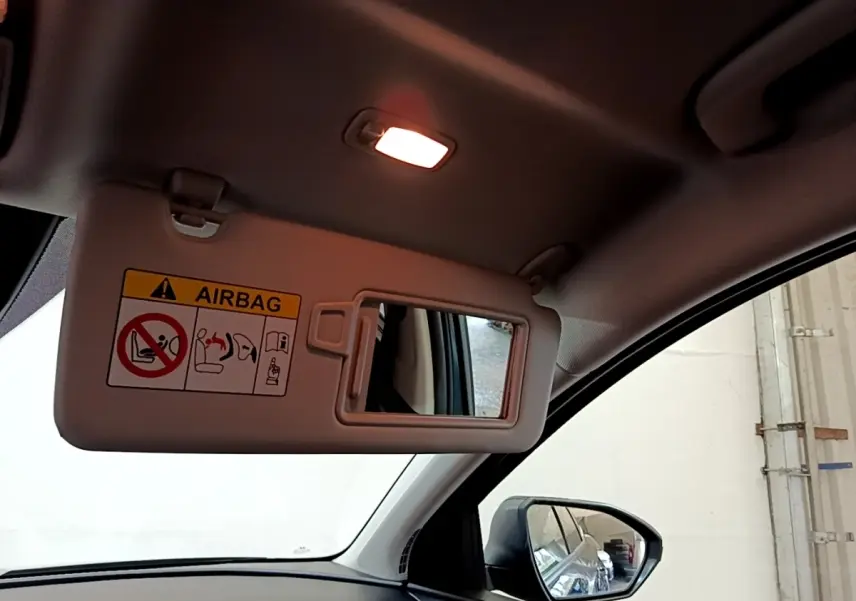 Vue intérieure côté conducteur du pare-soleil avec miroir et avertissement airbag, rétroviseur extérieur visible.