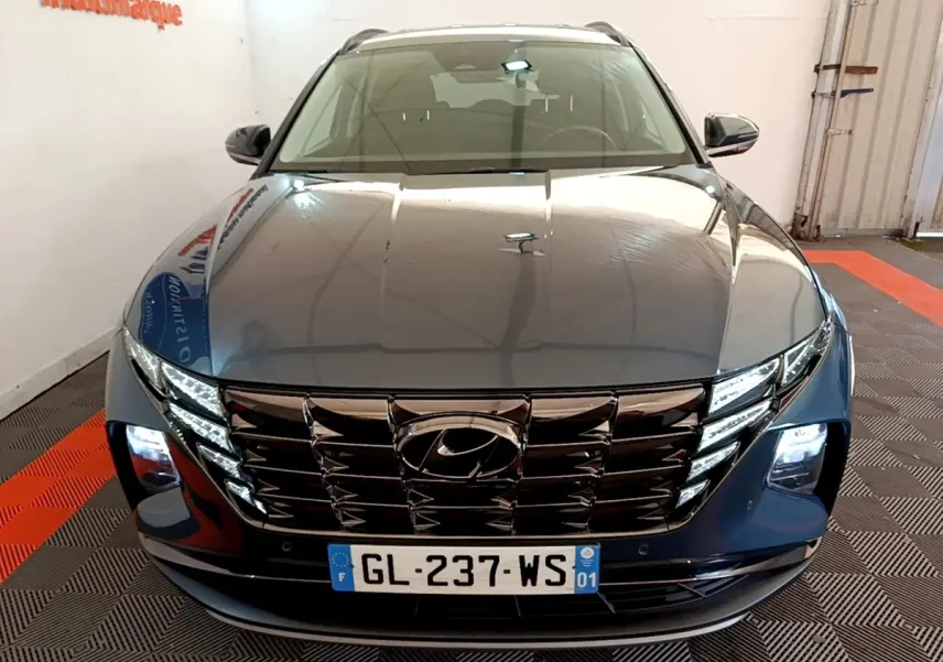 Vue avant d'un Hyundai Tucson bleu 2023 avec calandre chromée et phares LED allumés dans un showroom.