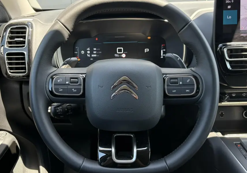 Vue rapprochée du volant noir de la Citroën C5 Aircross Hybrid 2025 avec commandes intégrées et tableau de bord numérique.
